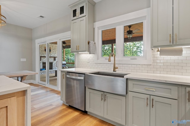 kitchen with dishwasher, sink, light wood-type flooring, tasteful backsplash, and light stone counters