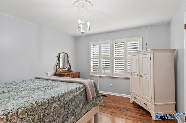 bedroom featuring an inviting chandelier, baseboards, wood finished floors, and visible vents