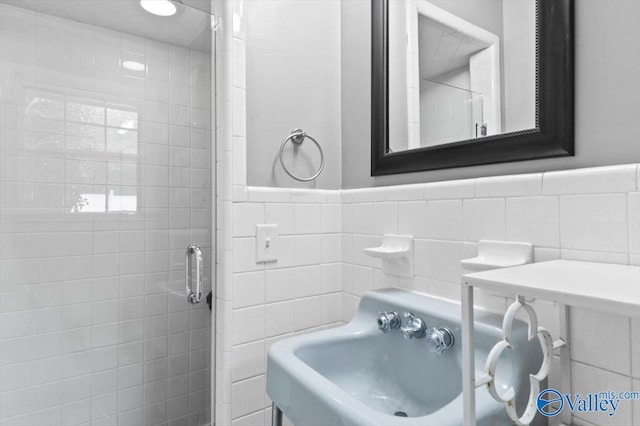 full bathroom with a wainscoted wall, a sink, a stall shower, and tile walls