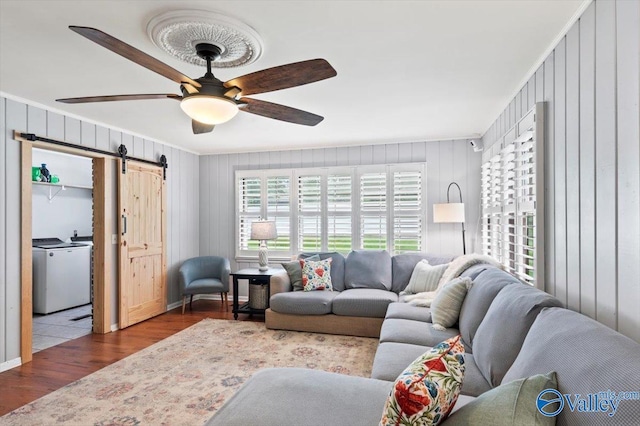 living room featuring ceiling fan, a barn door, wood finished floors, wooden walls, and ornamental molding