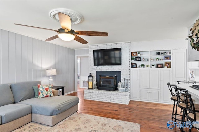 living area with ornamental molding, a ceiling fan, wood finished floors, and a brick fireplace