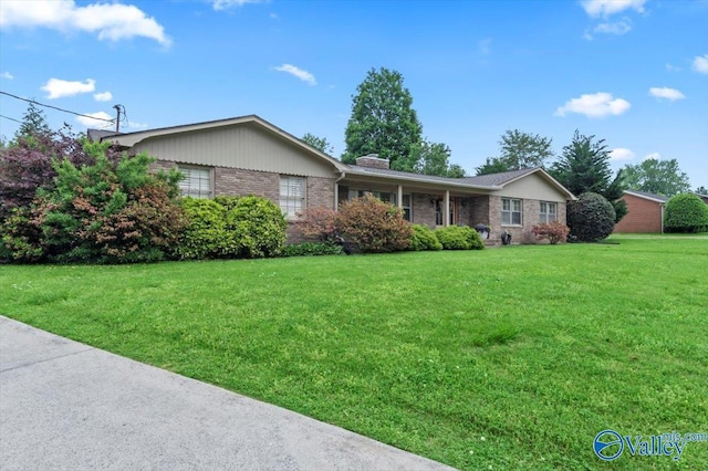 single story home featuring brick siding, a chimney, and a front yard