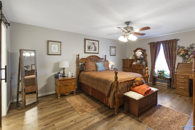 bedroom featuring light wood finished floors, a barn door, ceiling fan, a textured ceiling, and baseboards