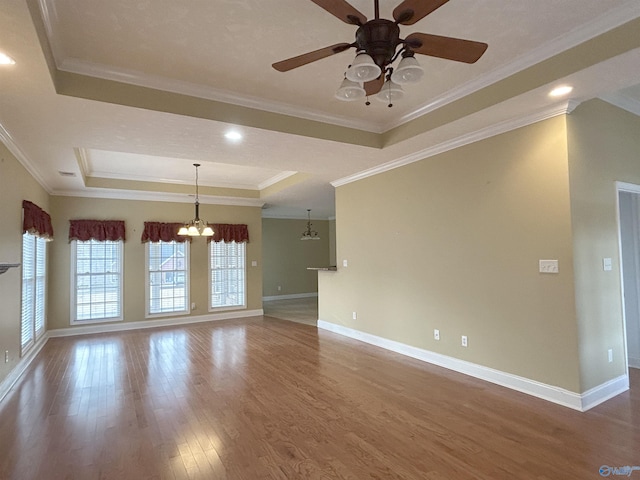 empty room with a raised ceiling, crown molding, ceiling fan with notable chandelier, and hardwood / wood-style floors