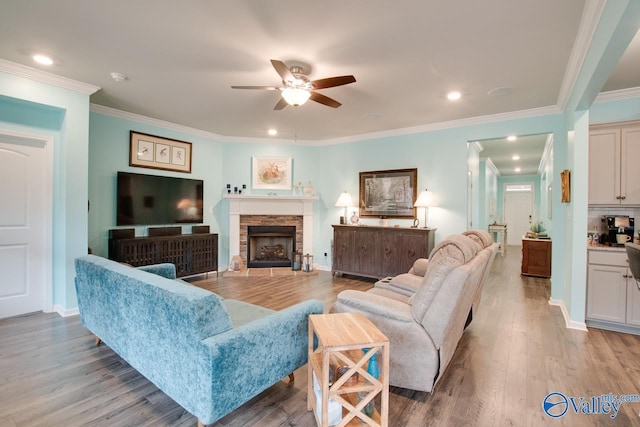 living area featuring ornamental molding, a ceiling fan, wood finished floors, a stone fireplace, and baseboards