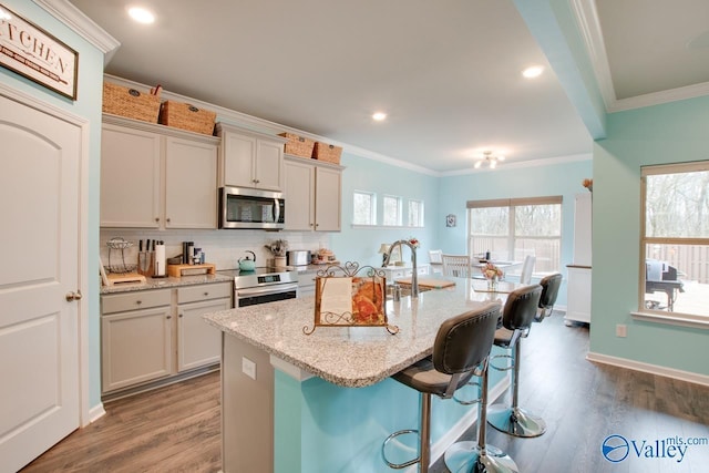 kitchen featuring a kitchen bar, appliances with stainless steel finishes, crown molding, and wood finished floors