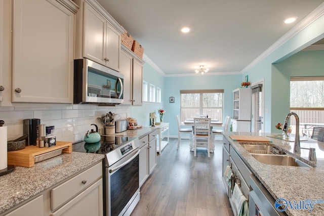 kitchen with a sink, stainless steel appliances, light wood-style floors, crown molding, and tasteful backsplash