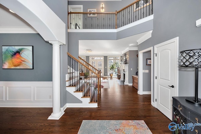 entryway featuring stairway, ornamental molding, wood finished floors, a high ceiling, and ornate columns