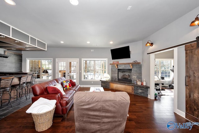 living area featuring a barn door, french doors, wood finished floors, a stone fireplace, and recessed lighting