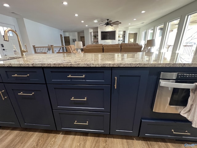 kitchen featuring blue cabinets, sink, light stone counters, light wood-type flooring, and oven