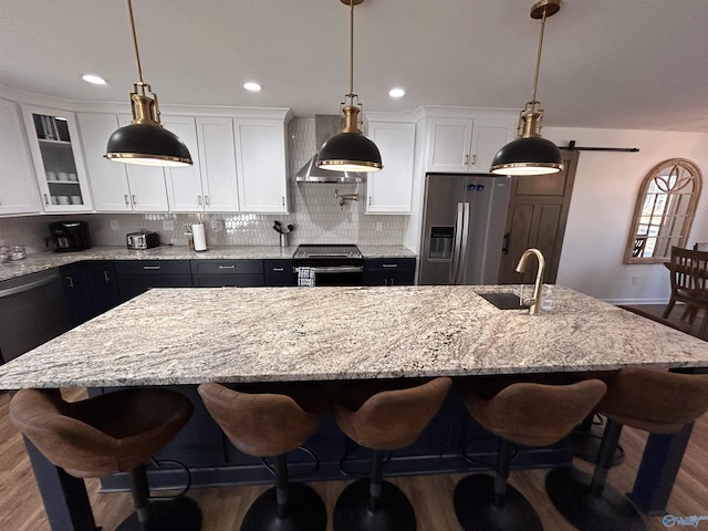 kitchen with white cabinetry, hanging light fixtures, a center island with sink, appliances with stainless steel finishes, and a barn door