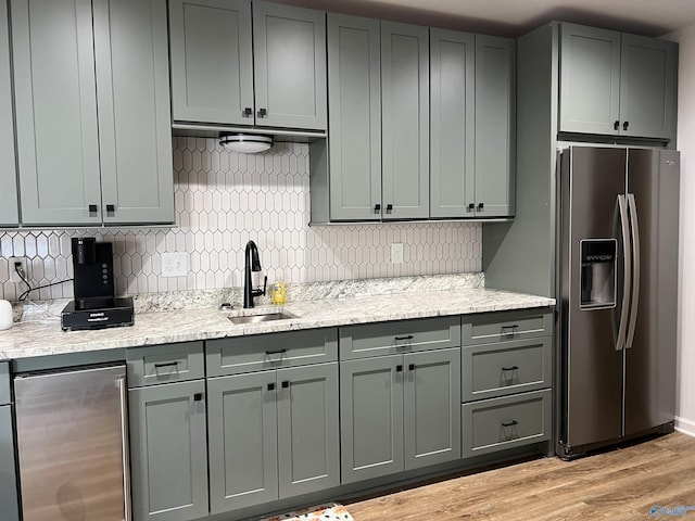 kitchen with sink, light stone counters, tasteful backsplash, stainless steel fridge with ice dispenser, and light hardwood / wood-style flooring