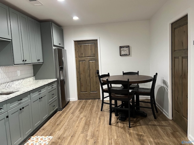 kitchen featuring gray cabinetry, stainless steel fridge with ice dispenser, light stone counters, and light wood-type flooring