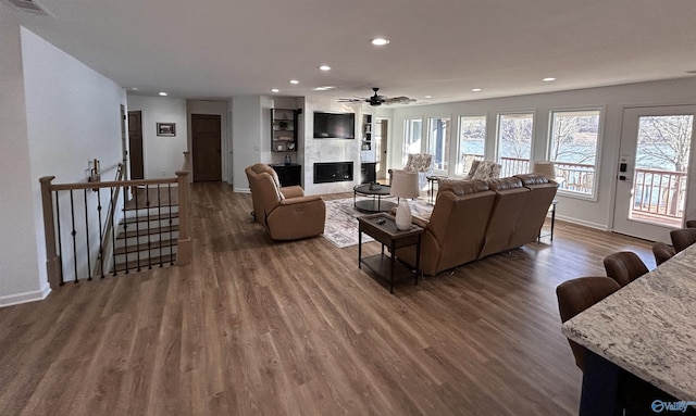 living room featuring ceiling fan, a large fireplace, wood-type flooring, and plenty of natural light