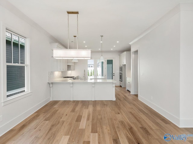 kitchen featuring light hardwood / wood-style flooring, tasteful backsplash, white cabinets, decorative light fixtures, and kitchen peninsula