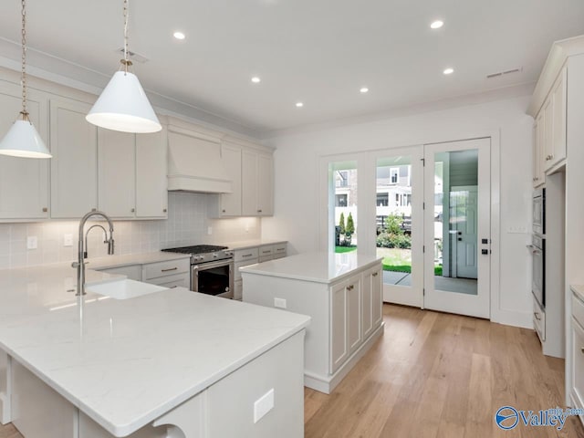 kitchen with premium range hood, sink, hanging light fixtures, appliances with stainless steel finishes, and a kitchen island