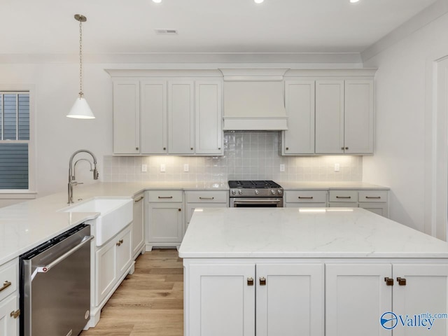 kitchen with appliances with stainless steel finishes, white cabinetry, sink, hanging light fixtures, and light stone counters