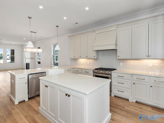 kitchen featuring appliances with stainless steel finishes, hanging light fixtures, a center island, custom exhaust hood, and kitchen peninsula