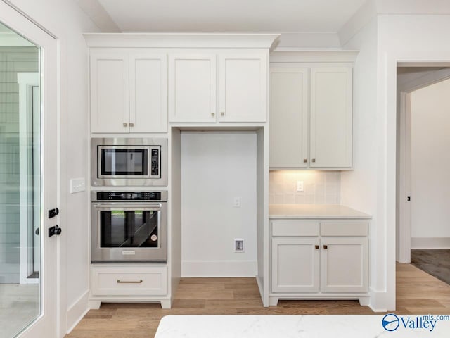 kitchen featuring white cabinetry, decorative backsplash, stainless steel appliances, and light wood-type flooring