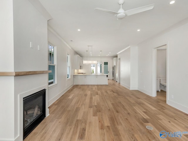 unfurnished living room with ceiling fan, ornamental molding, and light wood-type flooring