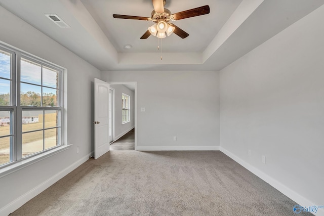 spare room featuring a tray ceiling, carpet flooring, visible vents, and baseboards