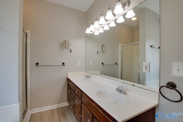 full bath with double vanity, wood finished floors, a shower stall, and a sink
