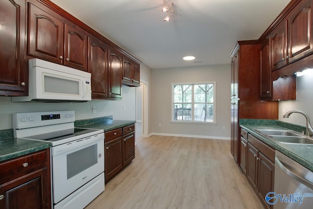 kitchen featuring a sink, dark countertops, baseboards, light wood-type flooring, and white appliances