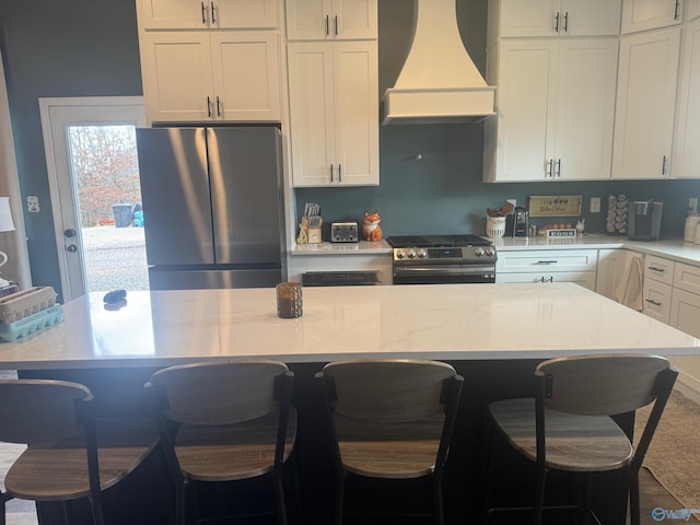 kitchen featuring stainless steel appliances, custom range hood, and a kitchen bar