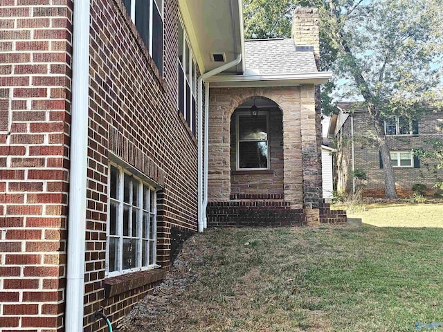 view of side of home with brick siding, a chimney, a shingled roof, and a yard