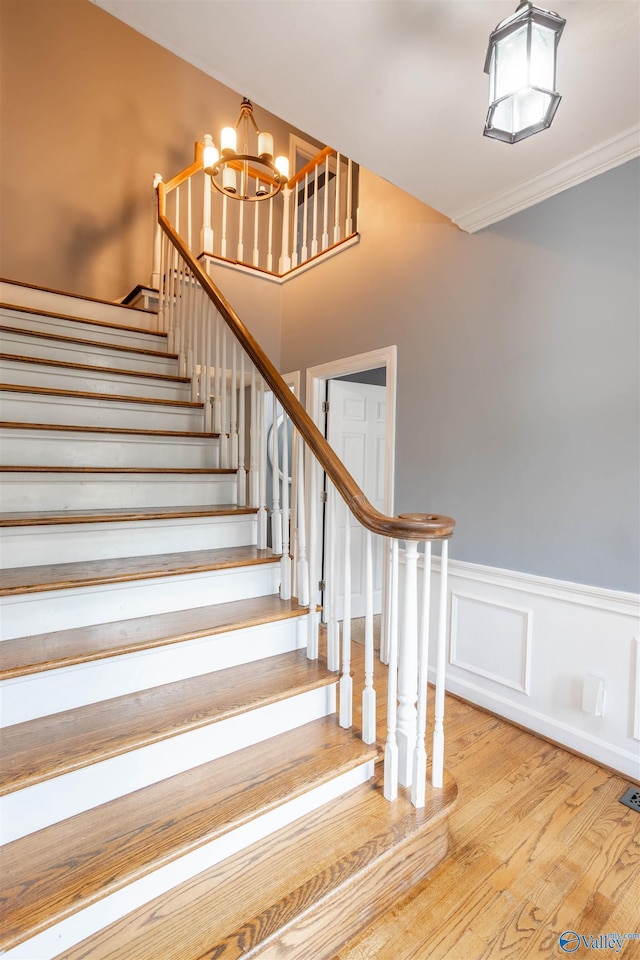 staircase with hardwood / wood-style flooring, crown molding, and a notable chandelier