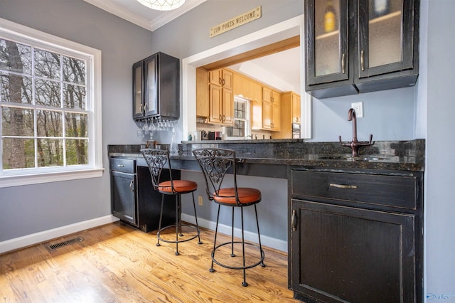 kitchen with sink, a kitchen breakfast bar, light hardwood / wood-style flooring, crown molding, and dark stone counters