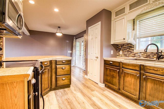 kitchen featuring a sink, decorative backsplash, tile counters, black range with electric cooktop, and stainless steel microwave