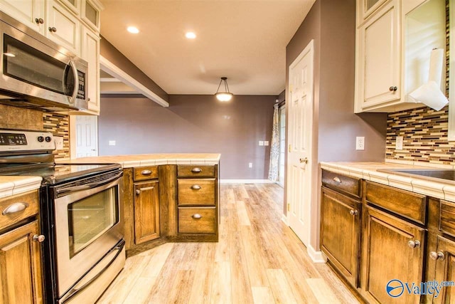 kitchen featuring brown cabinets, tile countertops, light wood-style floors, appliances with stainless steel finishes, and decorative backsplash