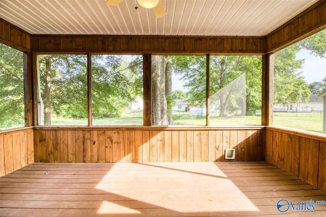 unfurnished sunroom featuring a deck, hardwood / wood-style floors, wooden walls, wooden ceiling, and ceiling fan