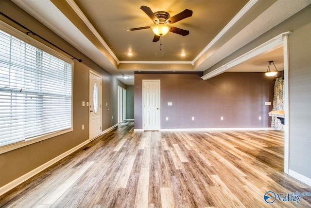 unfurnished living room with baseboards, a raised ceiling, ceiling fan, and ornamental molding
