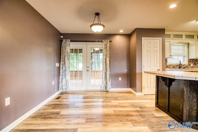 unfurnished dining area featuring a sink, french doors, baseboards, and light wood-style floors