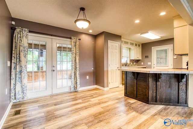 kitchen with visible vents, tile countertops, light wood-type flooring, french doors, and white cabinets