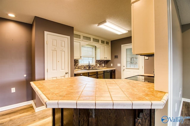 kitchen with tile countertops, a sink, black dishwasher, light wood-type flooring, and backsplash