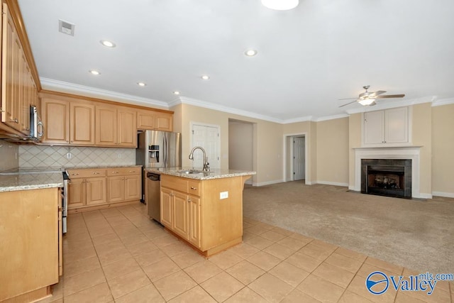 kitchen with ceiling fan, a tiled fireplace, appliances with stainless steel finishes, light tile patterned floors, and a center island with sink