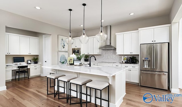 kitchen featuring appliances with stainless steel finishes, wall chimney exhaust hood, a sink, a breakfast bar, and wood finished floors