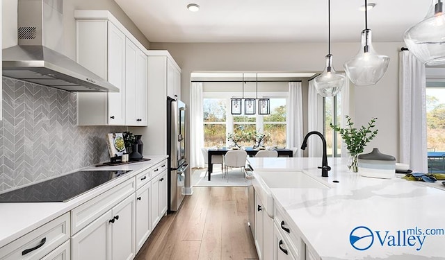 kitchen with wall chimney exhaust hood, stainless steel refrigerator, black electric stovetop, light countertops, and recessed lighting