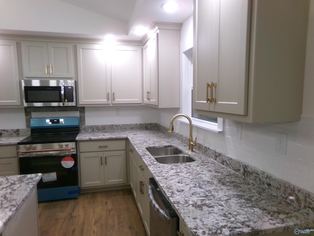 kitchen with light stone countertops, appliances with stainless steel finishes, dark wood-type flooring, sink, and lofted ceiling