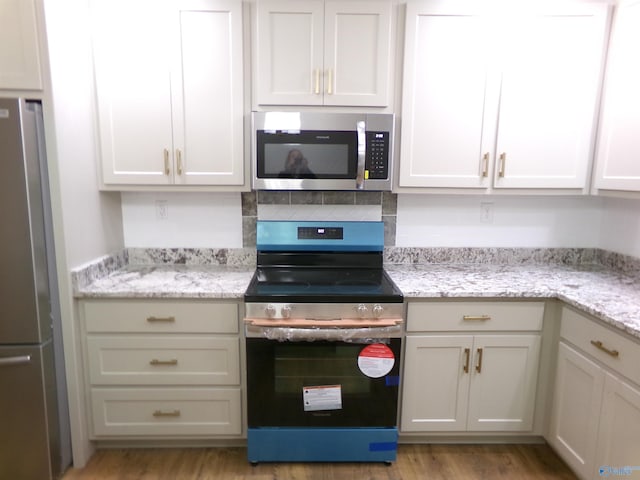 kitchen featuring light stone countertops, decorative backsplash, light wood-type flooring, stainless steel appliances, and white cabinets