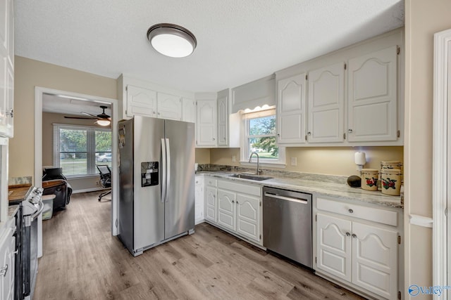 kitchen featuring appliances with stainless steel finishes, white cabinetry, light wood-type flooring, ceiling fan, and sink