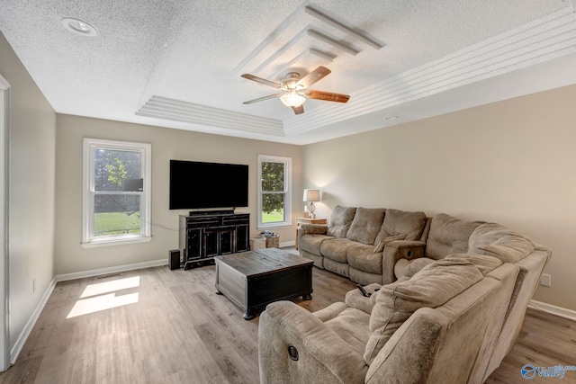 living room featuring ceiling fan, a raised ceiling, light hardwood / wood-style floors, and a healthy amount of sunlight