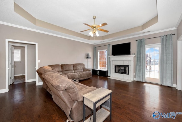 living area featuring dark wood-style floors, a tray ceiling, baseboards, and a tile fireplace