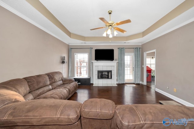 living area featuring a fireplace, a raised ceiling, dark wood-type flooring, a ceiling fan, and baseboards