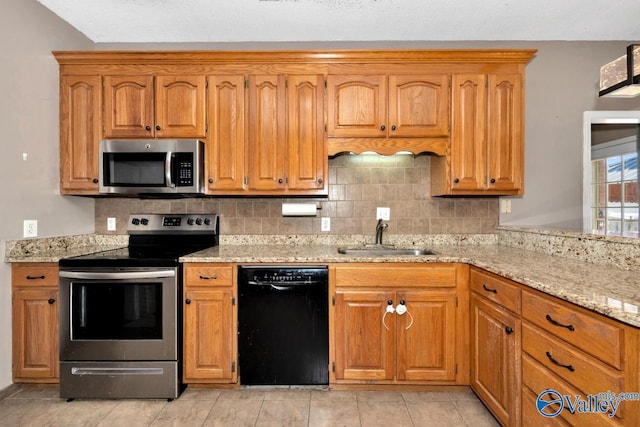 kitchen featuring light stone counters, backsplash, appliances with stainless steel finishes, brown cabinetry, and a sink