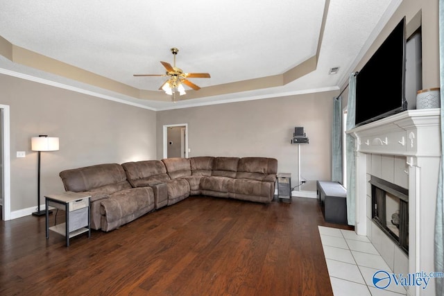 living room featuring a tiled fireplace, a ceiling fan, a raised ceiling, and wood finished floors