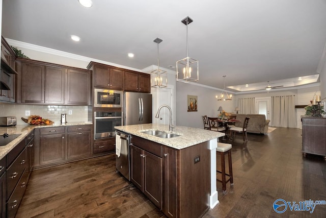 kitchen with appliances with stainless steel finishes, sink, hanging light fixtures, dark wood-type flooring, and a kitchen island with sink